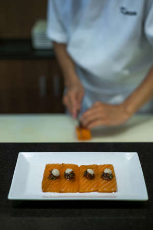 The chef prepares salmon sashimi. The process of making and decorating salmon sashimi. Salmon sashimi on white plate. Japanese traditional food.の写真素材