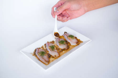 Sea bass sashimi with soy sauce on white plate isolated on white background. Hand pouring sauce on sea bass sashimi. Sushi in Japanese restaurant.の写真素材