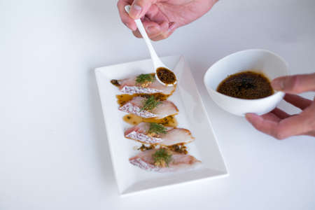 Sea bass sashimi with soy sauce on white plate isolated on white background. Hand pouring sauce on sea bass sashimi. Sushi in Japanese restaurant.の写真素材