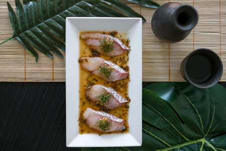 Sea bass sashimi with sauce on white plate, black decanter with sake and glass on the table. Japanese restaurant. Japanese traditional food. Raw fishの写真素材
