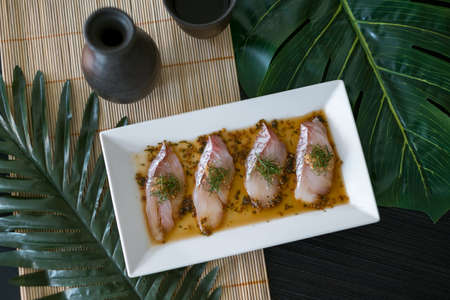 Sea bass sashimi with sauce on white plate, black decanter with sake and glass on the table. Japanese restaurant. Japanese traditional food. Raw fishの写真素材