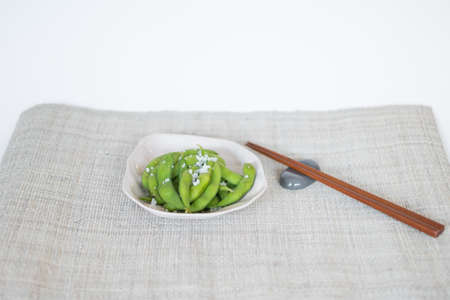 Green pea pods on white plate with wooden chopsticks on mat in Japanese restaurant, close-upの写真素材