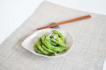 Green pea pods on white plate with wooden chopsticks on mat in Japanese restaurant, close-upの写真素材