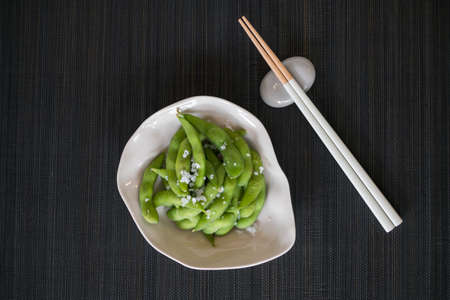 Green pea pods on white plate with wooden chopsticks on black mat in Japanese restaurant , close-upの写真素材
