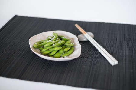 Green pea pods on white plate with wooden chopsticks on black mat in Japanese restaurant , close-upの写真素材