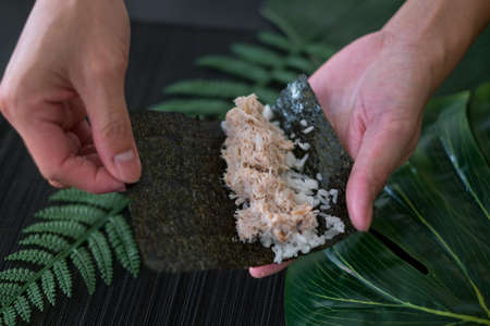 The process of making and decorating tuna Temaki Hand Roll. Hand Cooking Temaki Tuna Sushi in Japanese restaurant. Black background with green plantsの写真素材