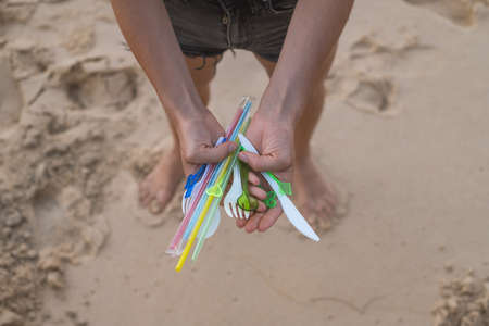 Hands holding used plastic dishes and straws on the beach. Sand on the background. Plastic pollution, Environmental Problem. Say no plastic.の写真素材
