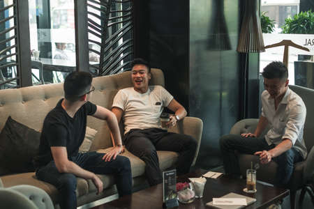 Three asian young men sitting in coffee shop, drinking coffee, talking and laughing. Design in...