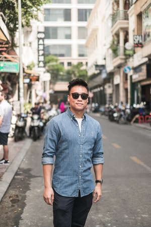 Portrait of asian young handsome man in denim shirt and sunglasses standing on the street and looking at camera with copy space. Chinese peopleの写真素材
