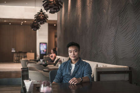 Asian young handsome man sitting in coffee shop and smiling. Chinese guy, millennials life, lifestyle in the big city, Modern Asia, coffee breakの写真素材