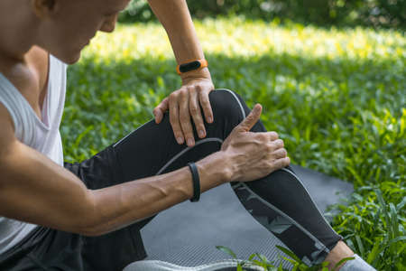 Close-up photo of man touching his knee with his hand. Man injured his knee. Sporty fit active young caucasian man in sportswear sittingの写真素材