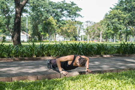 Sporty active young man in black sportswear doing sport exercises in the park. Fit caucasian man...