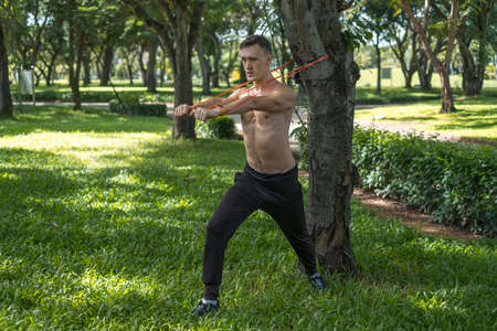Sporty active young man in black sportswear doing sport exercises in the park. Muscular fit man...