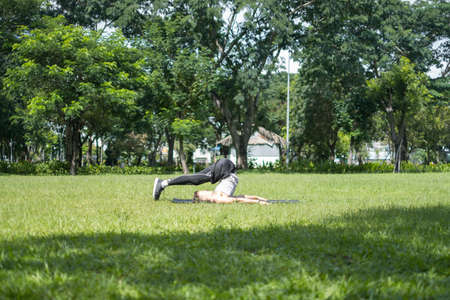 Sporty active young man in sportswear doing sport exercises in the park. Fit caucasian man stretching on the black sports mat outdoors.の写真素材