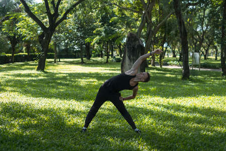 Sporty active young man in black sportswear doing sport exercises in the park. Portrait of handsome fit man doing stretching exercise outdoors.の写真素材