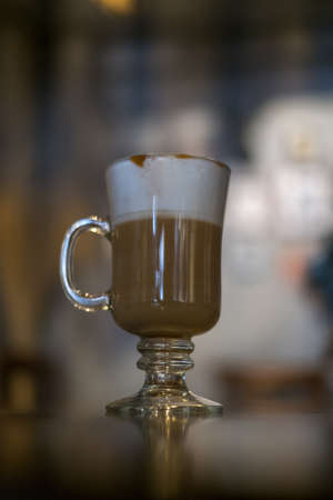 Glass cup with latte is on the table in coffee shop. Glass with caramel cappuccino on the table in the restaurant. Photo for the menu, advertisingの写真素材