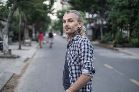 Portrait of mature handsome man in shirt and jeans walking on the street in asia. Long grey hair. Portrait. High quality photoの写真素材