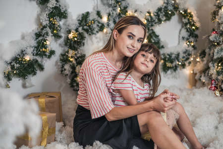Christmas studio family shoot. New Years photo of happy family. Beautiful Mother and cute daughter hugging each other and smilingの写真素材