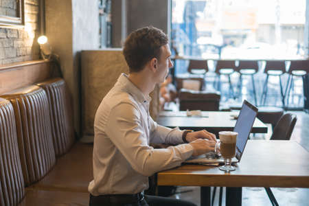 Freelancer working in coffee shop with a laptop. Thinking, solving problems, new ideas. Young business man surfing the net on laptop in a bar.の写真素材