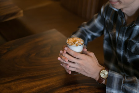 Man in checkered shirt drinks coffee in a bar. Holding caramel latte in his hands. Close up, Coffee shop, cafe, latte, caramel cappuccino.の写真素材
