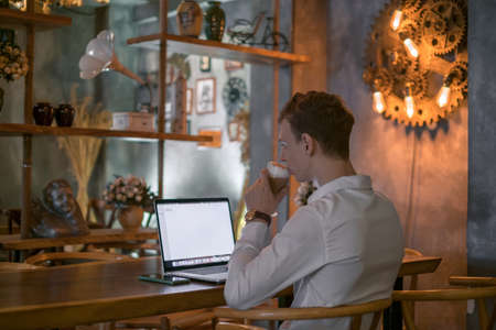 Young caucasian business man surfing the net on laptop while drinking coffee in a bar. Handsome man...
