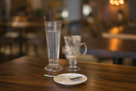 Two empty iced coffee glass cups on the table in coffee shop and white saucer with a spoon. High...