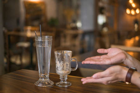 Two empty iced coffee glass cups on the table in coffee shop and hands showing on glasses. High quality photoの写真素材