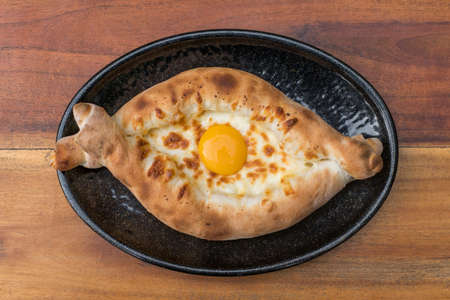 Traditional Georgian cuisine. Ajara khachapuri with egg on black plate on wooden background Top view, close up with copy space. High quality photoの写真素材