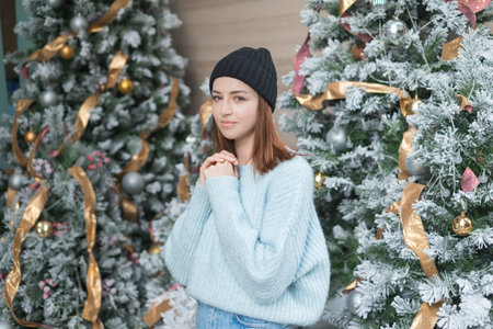 New Year portrait of beautiful smiling caucasian young woman in cozy wool warm light blue sweater standing near decorated Christmas tree. happy personの写真素材