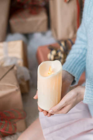 Woman in light blue sweater holding thick white wax candle in her hands. Christmas holiday. Female hands with wax candle. Copy space, close upの写真素材