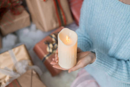 Woman in light blue sweater holding thick white wax candle in her hands. Christmas holiday. Female hands with wax candle. Copy space, close upの写真素材