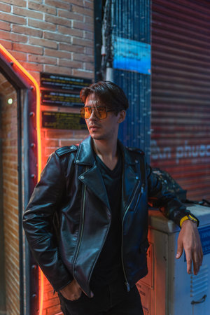 Portrait of young stylish brunet caucasian man in black leather jacket and yellow sunglasses....