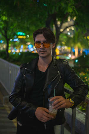 Portrait of young handsome brunet caucasian man in black leather jacket and yellow sunglasses....