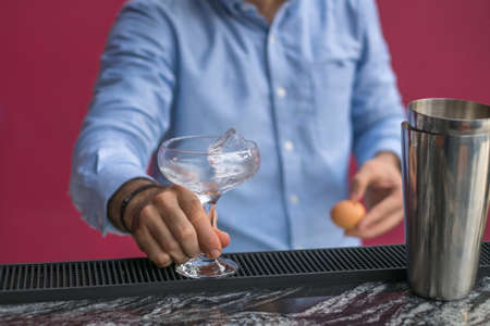 Bartender cools the glass with ice before making a cocktail. Close up photo, process, bar. High...