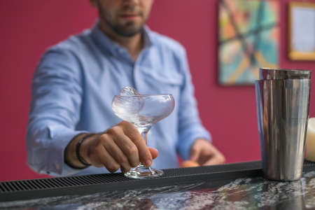 Bartender cools the glass with ice before making a cocktail. Close up photo, process, bar. High...