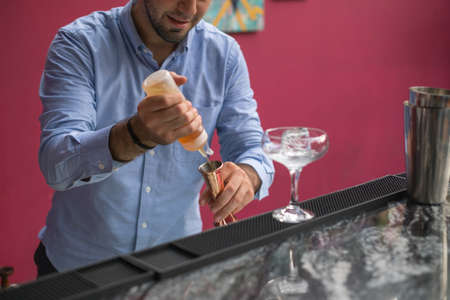 Bartender makes cocktail in mister glass. Close up photo, process, bar, Pink wall, restaurant. High quality photo.の写真素材