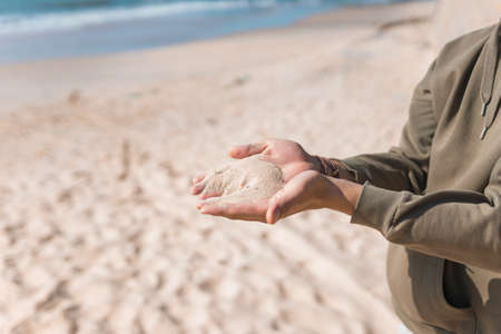 Man holding white sand in his hands. Male palms with the sand on the beach. Sand pouring. Casual hoodies. high quality photoの写真素材