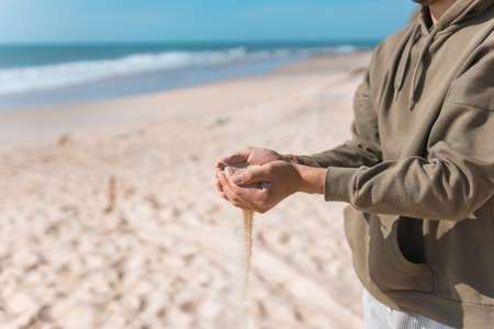 Man holding white sand in his hands. Male palms with the sand on the beach. Sand pouring. Casual hoodies. high quality photoの写真素材