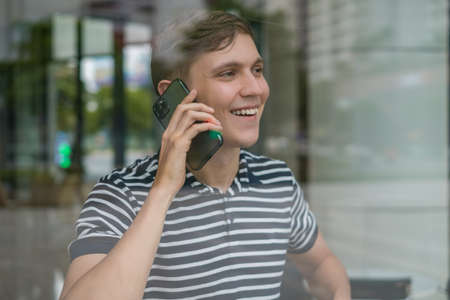 Portrait of young caucasian man in casual clothes making phone call. Photo through the glass. Using smartphone, talking by the phone. Urban lifestyle.の写真素材