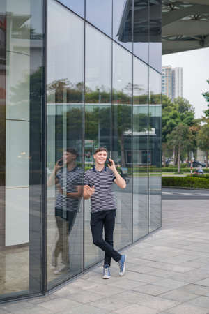 Portrait of young caucasian man in casual clothes standing outdoors and making phone call. Using...