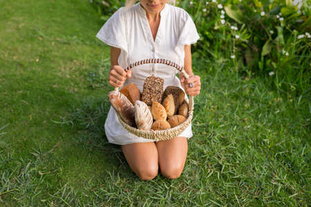 Young woman in white dress sitting on the grass with basket with assorti of brown and white homemade...