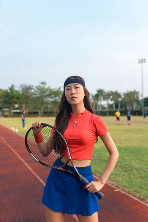 Asian young woman with black headband standing on the tennis court and holding tennis racket. High quality photoの写真素材