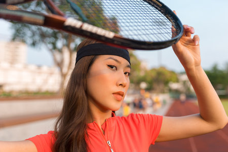 Asian young woman with black headband standing on the tennis court and holding tennis racket. High quality photoの写真素材