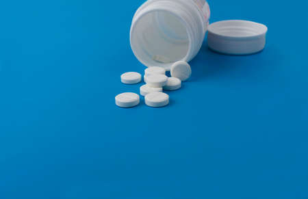 white tablets in a plastic jar with a lid, lying on an isolated blue backgroundの写真素材