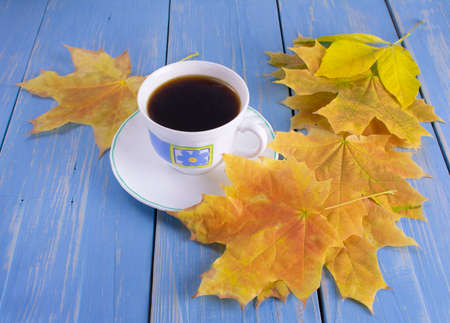 coffee Cup on a wooden blue background next to yellow leavesの写真素材