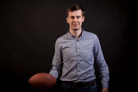 Dark-haired man in a plaid shirt 
holds a rugby ball in his hands on black isolated backgroundの写真素材