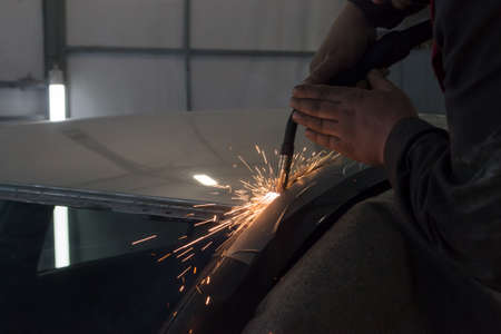 Experienced man performs work on body repair car with a welding machine. Repair of the roof of the...
