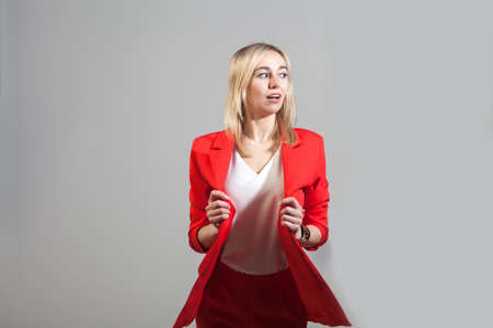 Young beautiful white blond girl in a bright red strict suit with a jacket and white blouse standing in a pose on a white isolated backgroundの写真素材