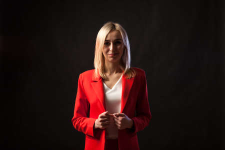 Young beautiful white blond girl in a bright red strict suit with a jacket and white blouse looks at...