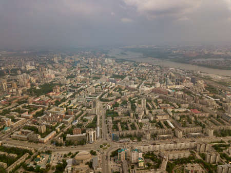 Aerial view of square in the city with roundabout traffic, streets and buildings with green trees. A lot of buildings in Novosibirsk with cloudy weather.の写真素材